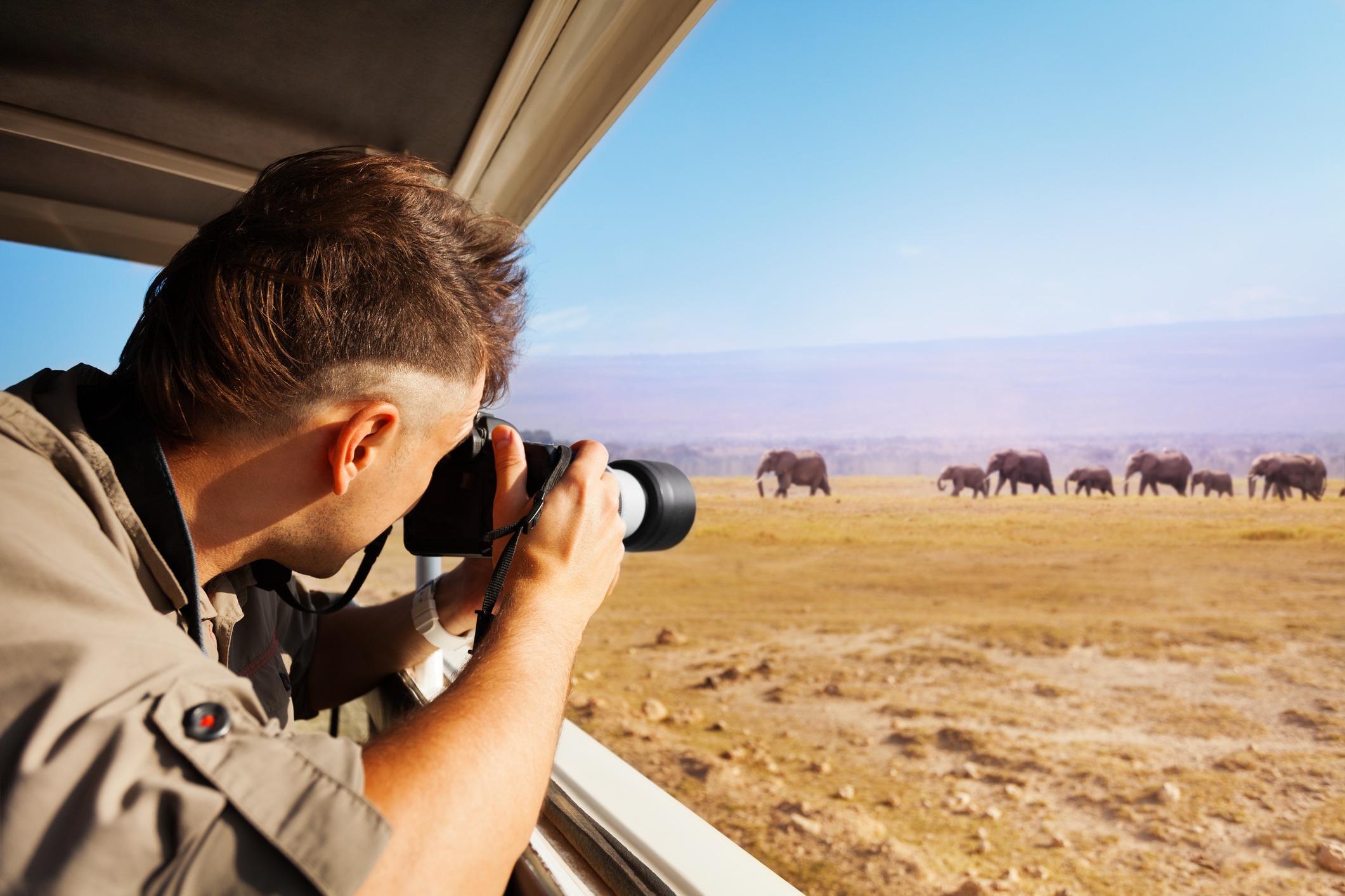 Man taking photo of herd of elephants during Great Migration from safari jeep, Kenya, Africa